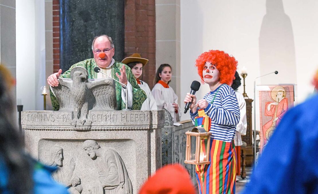 Ein Pfarrer mit roter Clown-­Nase predigt bei einem Karnevalsgottesdienst am 16. Februar 2020 in einer Kirche in Bonn. Neben dem Ambo steht ein Clown. (Foto: Harald Oppitz/KNA)